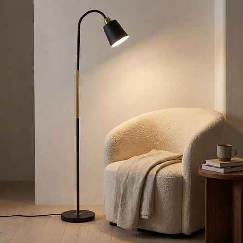 Furze black iron floor lamp lit beside a cream boucle armchair in a warm neutral living room
